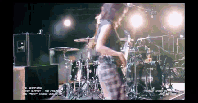 a woman playing a guitar in front of a drum set with the words the warning on the bottom