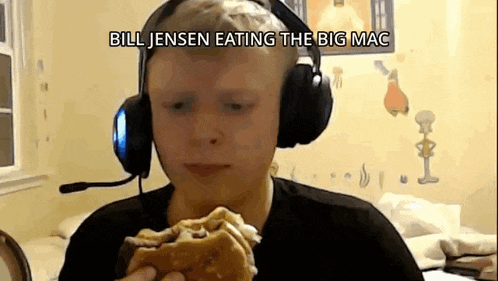 a young boy wearing headphones is eating a big mac sandwich .