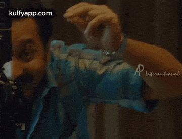 a man with a mustache is making a funny face while wearing a watch and a blue shirt .