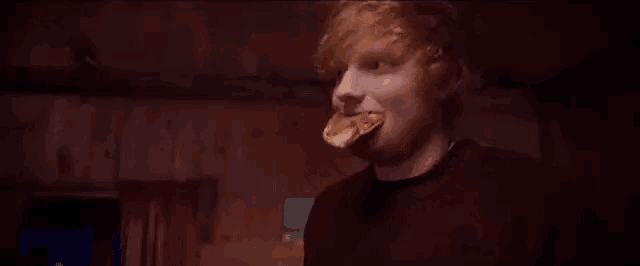 a man is eating a slice of pizza in a dark room .