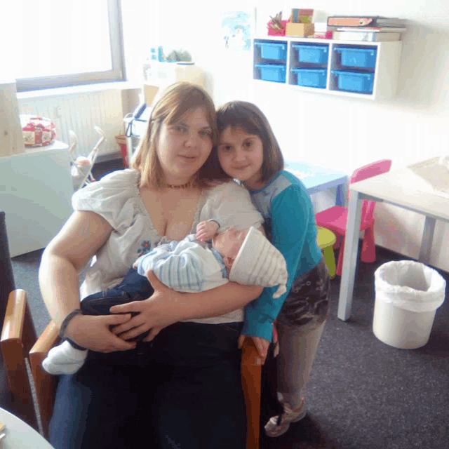 a woman is holding a baby in her arms while a little girl looks on