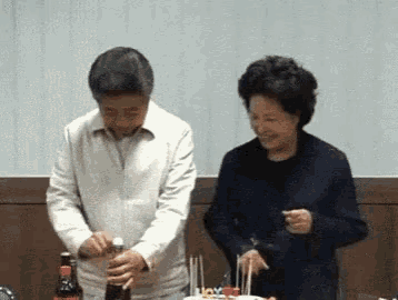 a man and a woman are standing next to a birthday cake