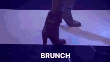 a woman is walking down a runway wearing high heels and the word brunch is visible behind her .