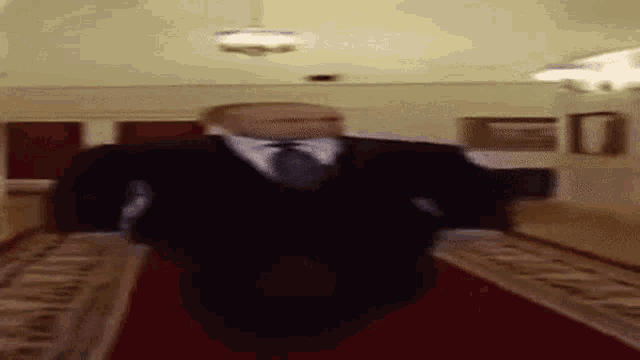 a blurry picture of a man in a suit and tie walking down a red carpet .