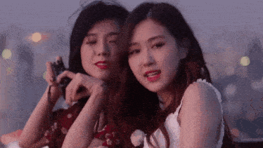 two young women are sitting next to each other on a rooftop . one is holding a camera .