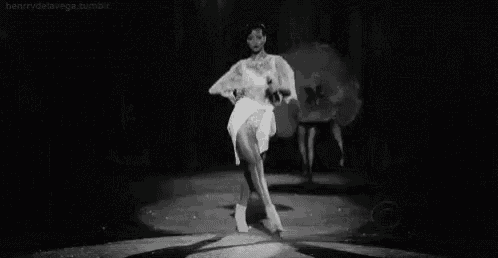 a black and white photo of a woman dancing on a stage at a fashion show .