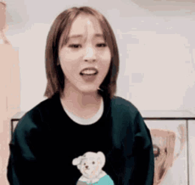 a woman wearing a black sweater with a teddy bear on it is standing in a room .
