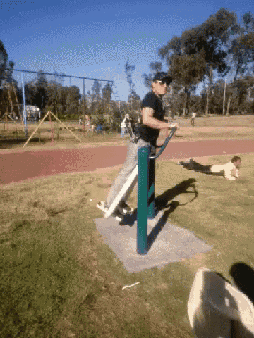 a man in a black shirt is doing exercises on a green pole in a park
