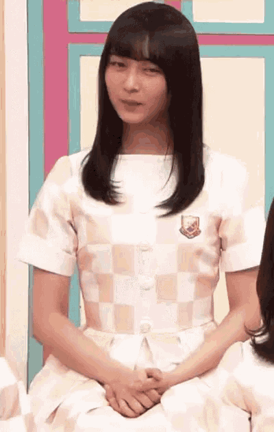 a woman in a white checkered shirt is sitting down with her hands folded