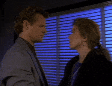a man and woman are kissing in front of a window