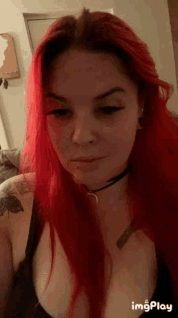 a woman with red hair is wearing a choker and has a tattoo on her shoulder .