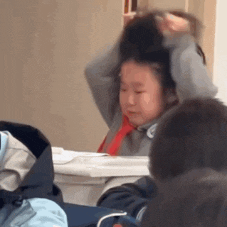 a girl is sitting at a desk in a classroom with her hands on her head .