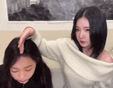 a woman in a white off the shoulder sweater is touching another woman 's head