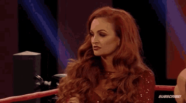 a woman with red hair is sitting in a boxing ring talking to a man .
