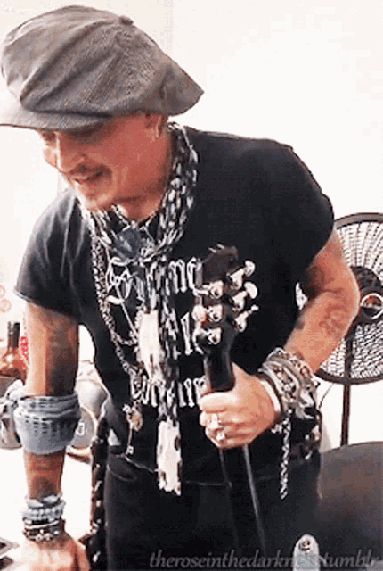 a man wearing a hat and a black shirt that says " come all " is holding a microphone