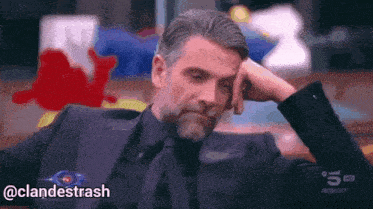 a man in a suit and tie is sitting with his head resting on his hand and the hashtag @clandestrash is below him