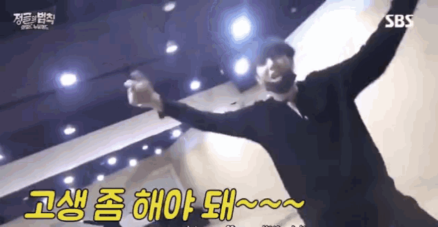a man is dancing in a room with his arms outstretched and says sbs in the background .