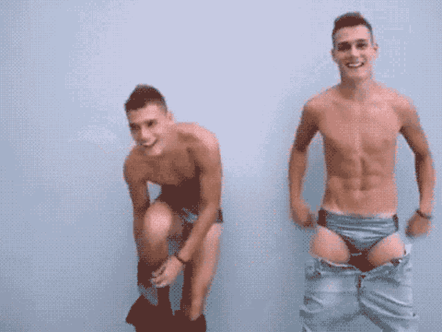 two shirtless men are standing next to each other and one is taking off his pants