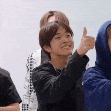 a young boy is giving a thumbs up sign while sitting in a room with other people .