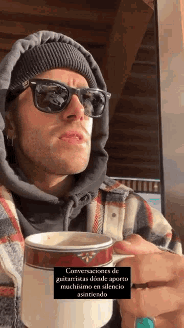 a man wearing sunglasses and a hooded jacket is holding a cup of coffee .