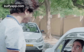a man is standing next to a car talking to another man .