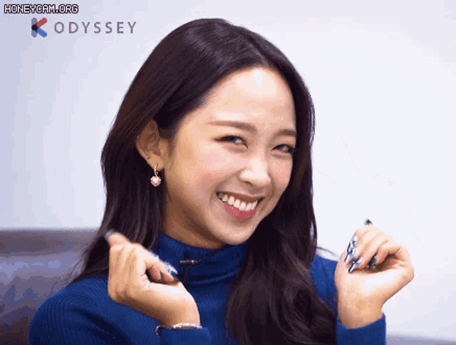 a woman wearing a blue sweater and earrings is smiling in front of a honeycam org logo