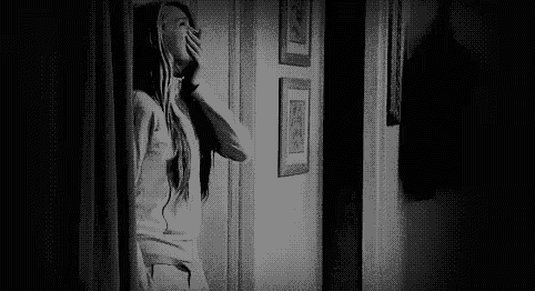 a black and white photo of a woman looking out of a doorway .