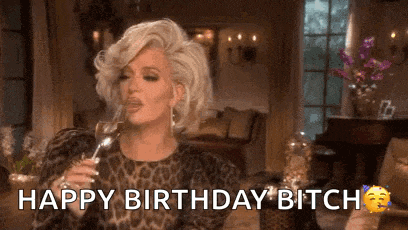 a woman in a leopard print dress is holding a glass of wine and says `` happy birthday bitch '' .