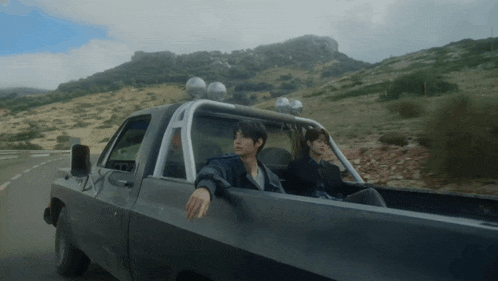 two men are sitting in the back of a truck on a road
