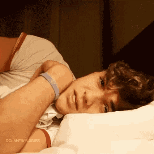 a young man is laying on a bed with his head on a pillow and looking at the camera .