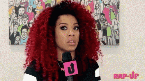a woman with red curly hair is talking into a microphone with the word rap-up on it .