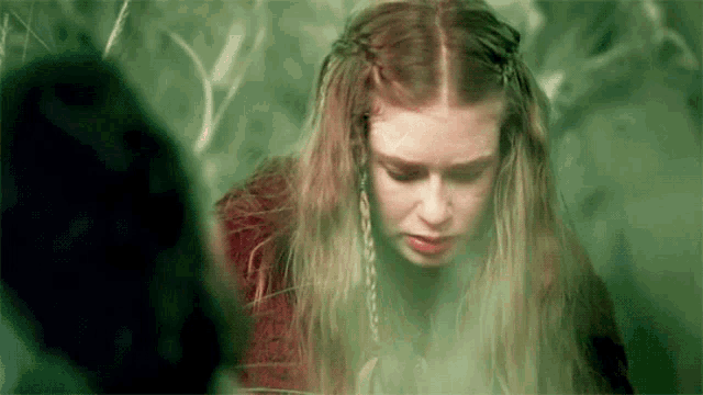 a woman with long hair and braids is standing in a forest .