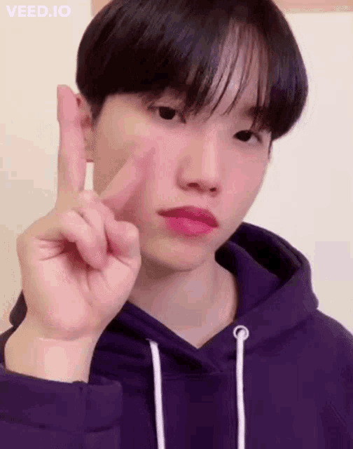 a young man is wearing a purple hoodie and making a peace sign with his finger .