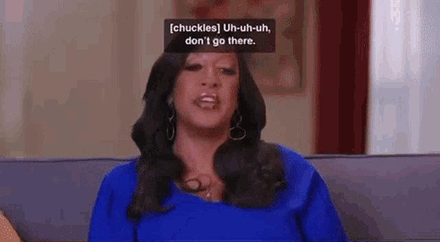 a woman in a blue dress is sitting on a couch talking to someone .