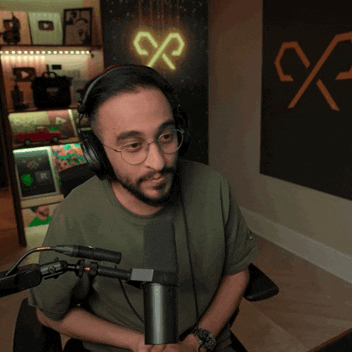 a man wearing headphones and glasses sits in front of a microphone in front of a sign that says x