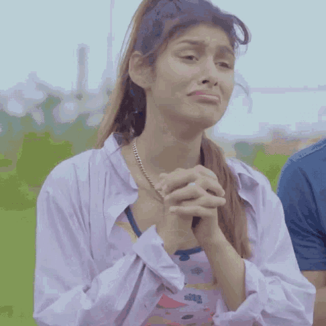 a woman in a purple shirt is praying with her hands folded in front of her face .