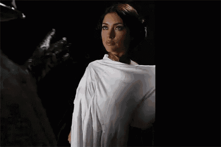 a woman in a white dress is standing in a dark room with a white cloth wrapped around her .