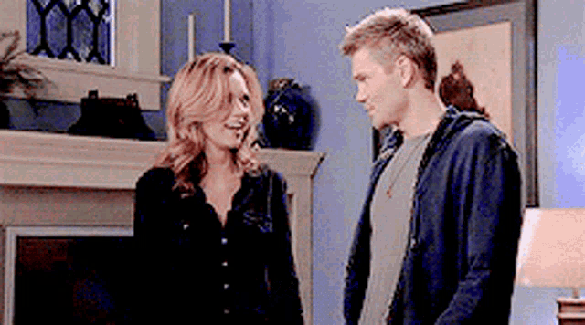 a man and a woman are standing next to each other in a living room looking at each other .
