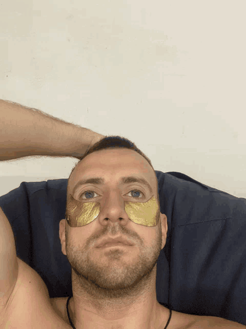 a shirtless man with gold eye patches on his face