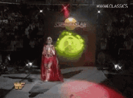 a wrestler in a red cape is walking down the aisle of a wrestling arena .