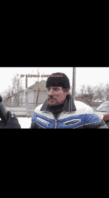 a man wearing a black hat and a blue jacket is being interviewed by someone