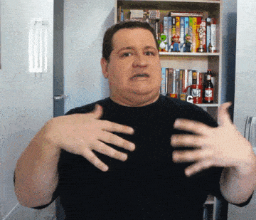 a man in a black shirt has his hands outstretched in front of a bookshelf with a mug that says " duff " on it