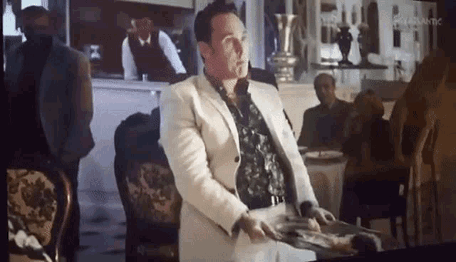 a man in a white suit is sitting at a table in a restaurant holding a plate of food .