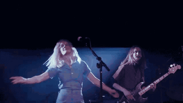 a woman singing into a microphone while a man plays a bass