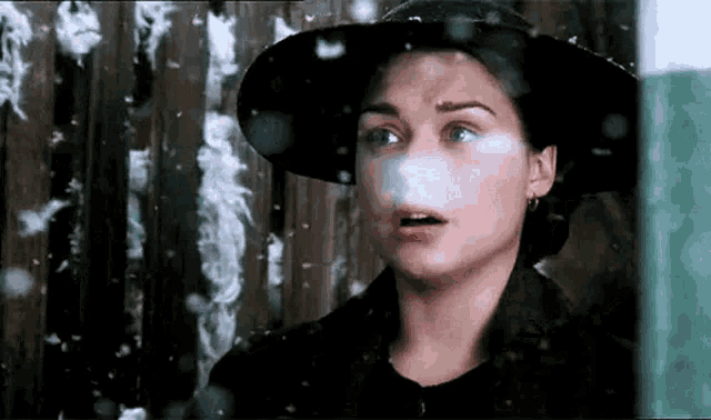 a woman wearing a black hat is looking out a window at the snow falling .