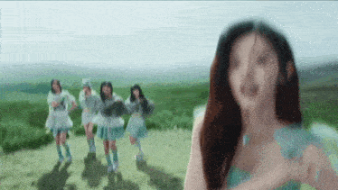 a group of girls are dancing in a field with a woman standing in the foreground .