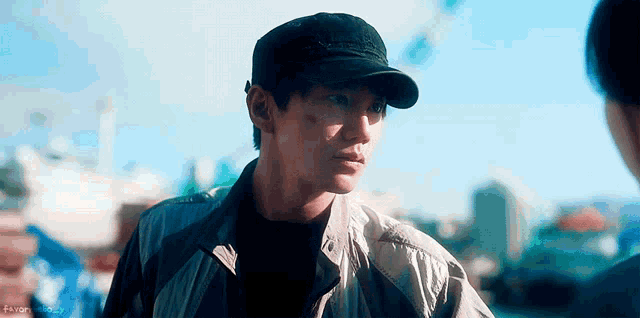a man wearing a baseball cap and a jacket is looking at another man .