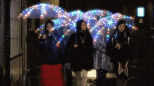 a group of people walking down a street with umbrellas that are lit up