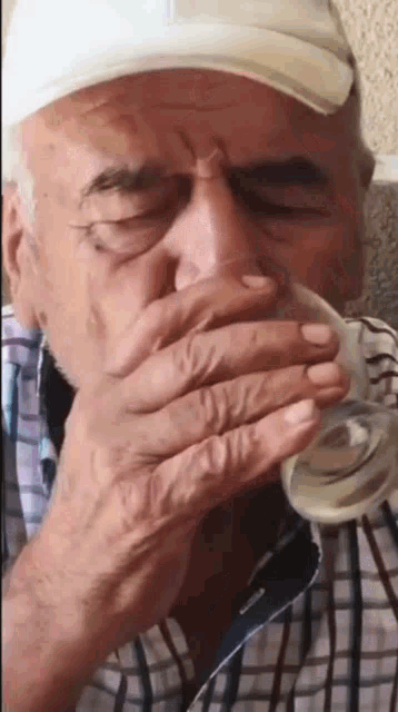 an elderly man is drinking a glass of water .