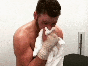 a shirtless man is blowing his nose with a towel in a bathroom .
